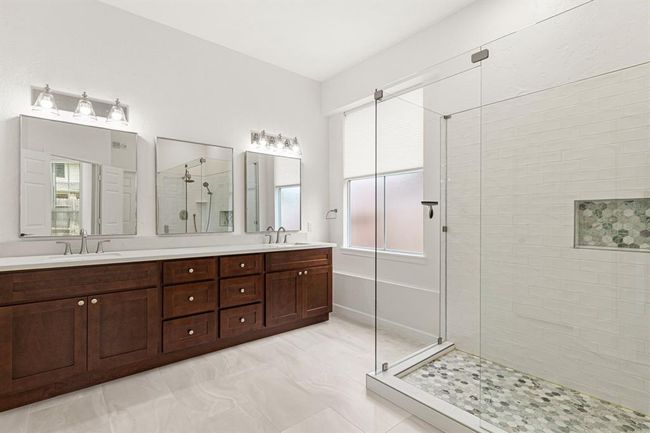 The remodeled primary bathroom has a new double vanity, mirrors, light fixtures, tile, and oversized shower with frameless glass enclosure and designer tile | Image 21