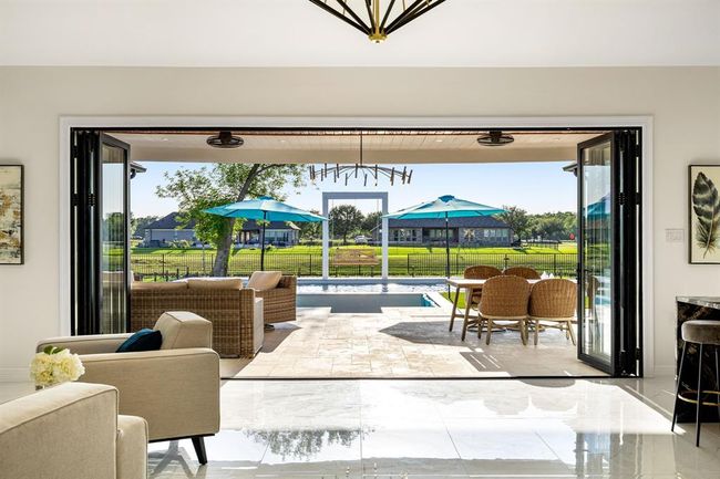 Experience true indoor-outdoor living with this beautifully designed space that opens up to a spacious covered patio, sparkling pool, and serene views of lush greenery beyond the fence line. Perfect for entertaining or relaxing in total tranquility. | Image 39