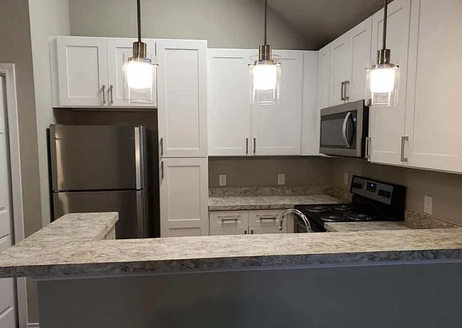 Kitchen with stainless steel appliances, lofted ceiling, white cabinets, decorative light fixtures, and a peninsula | Image 7