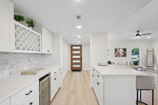 Kitchen featuring wine cooler, open floor plan, a kitchen bar, tasteful backsplash, and white cabinetry | Image 20