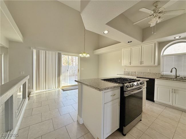 Kitchen with ceiling fan with notable chandelier, a sink, light stone counters, light tile patterned floors, and stainless steel gas range | Image 13