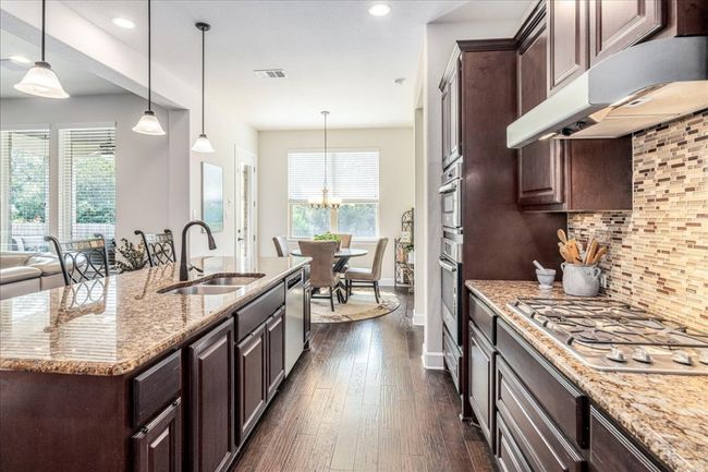 Kitchen with dark brown cabinets, stainless steel appliances, decorative backsplash, dark wood finished floors, and recessed lighting | Image 6