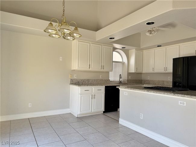 Kitchen with a notable chandelier, black appliances, a sink, white cabinetry, and light stone countertops | Image 8