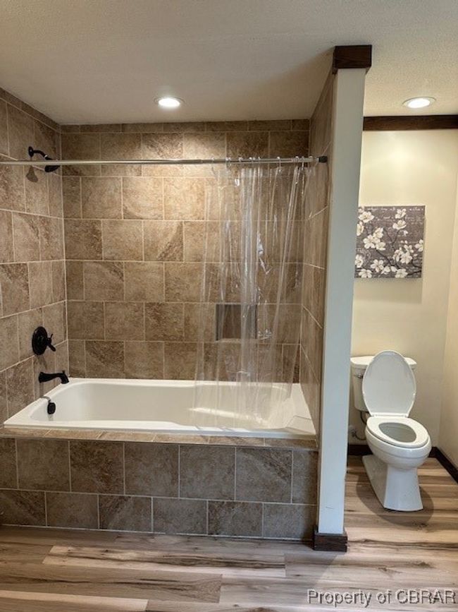 Bathroom featuring tiled shower / bath, toilet, and wood finished floors | Image 13