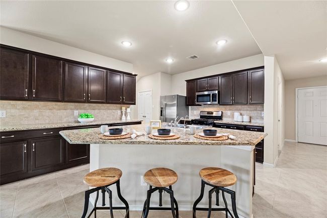 Your chef inspired kitchen awaits! Features include granite countertops paired with a coordinating stone backsplash, stainless steel appliances, rich cabinets with updated hardware, under cabinet lighting, recessed lighting, and a sprawling island with breakfast bar seating. | Image 4