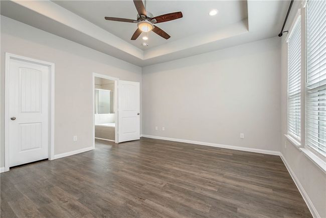 Unfurnished bedroom featuring a raised ceiling, dark wood-type flooring, ensuite bath, recessed lighting, and a ceiling fan | Image 12