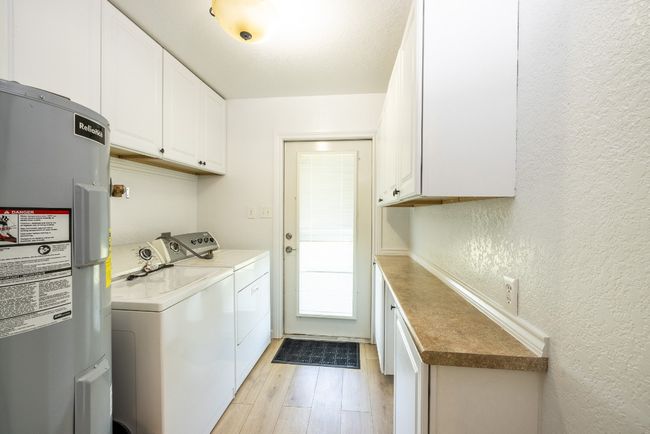 Washroom featuring a textured wall, electric water heater, light wood finished floors, cabinet space, and washer and clothes dryer | Image 25