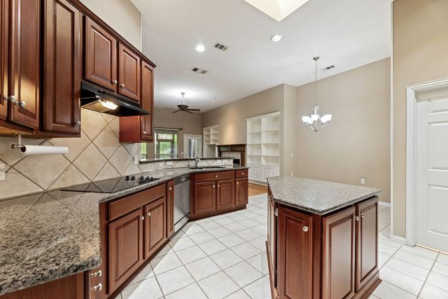 Kitchen with black electric stovetop, under cabinet range hood, stainless steel dishwasher, tasteful backsplash, and light tile patterned floors | Image 15