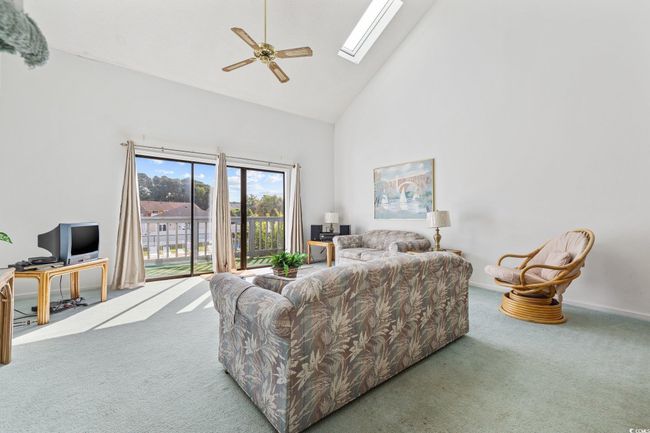 Carpeted living area featuring high vaulted ceiling, a ceiling fan, a skylight, and an office area | Image 4