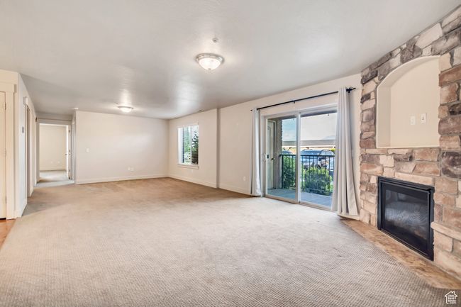 Unfurnished living room featuring a stone fireplace, light carpet, and plenty of natural light | Image 5