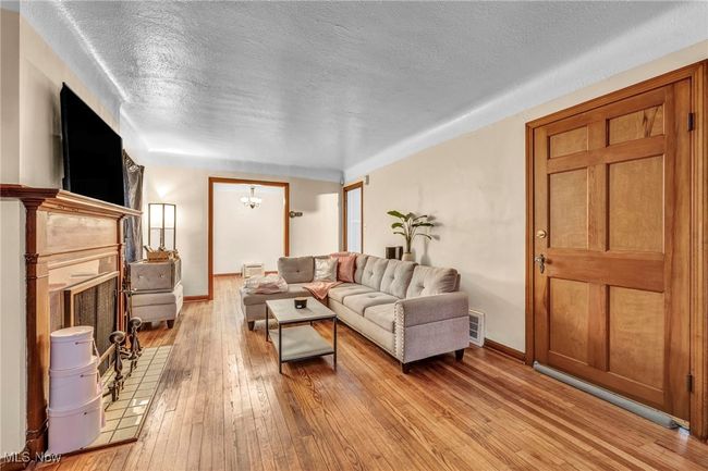 Living room featuring a textured ceiling, a fireplace with flush hearth, light wood-style flooring, baseboards, and visible vents | Image 8