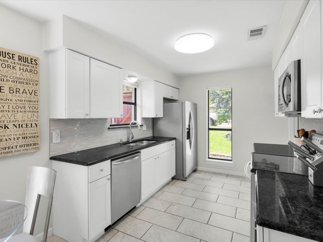 Kitchen with stainless steel appliances, tasteful backsplash, white cabinetry, and dark stone counters | Image 7