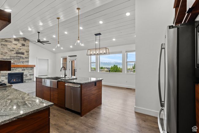 Kitchen with appliances with stainless steel finishes, a sink, a stone fireplace, a ceiling fan, and dark wood-type flooring | Image 10