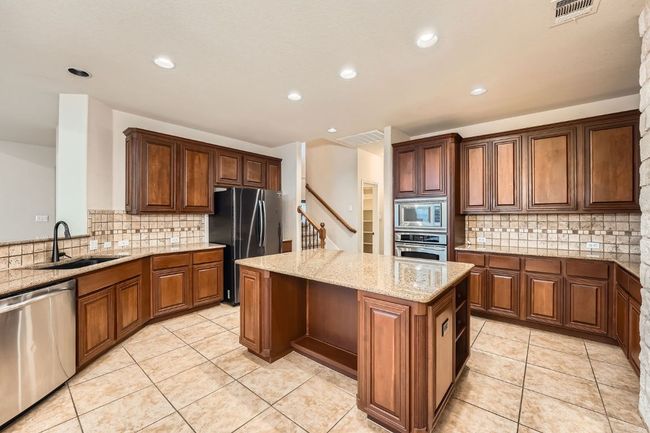Kitchen featuring visible vents, decorative backsplash, a kitchen island, a sink, and stainless steel appliances | Image 14