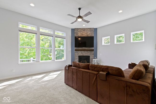 Added windows in the living room bring in tons of natural light and views of the woods behind. Electronic blinds can block out the light for those Sunday matinee movies! Gas fireplace with stacked stone surround and raised hearth for cozy evenings. | Image 14