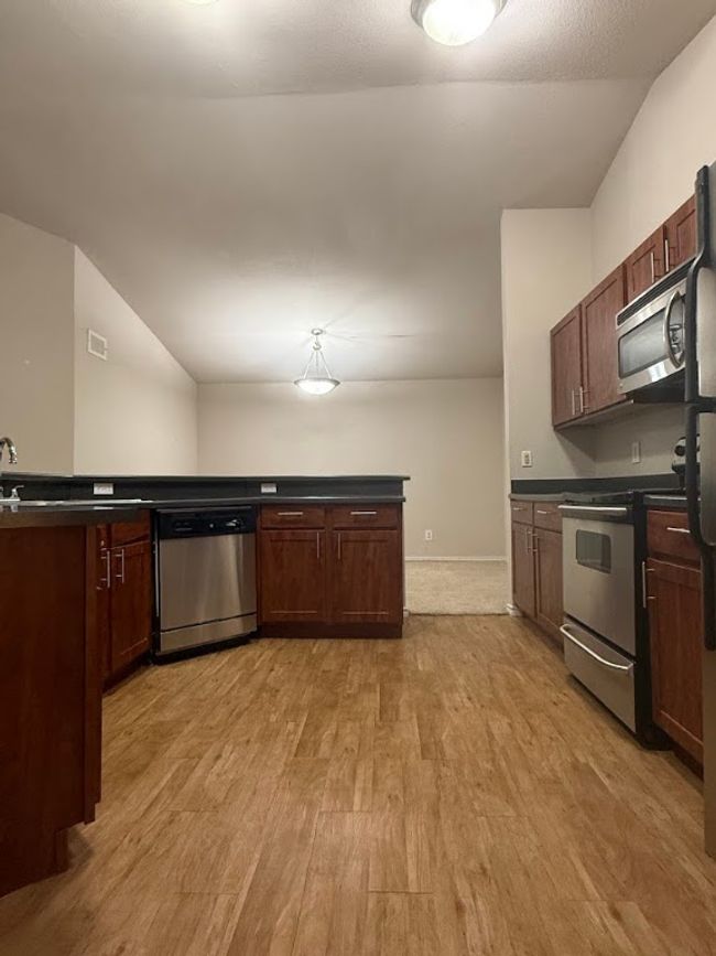 Kitchen with stainless steel appliances, light wood-style floors, and dark countertops | Image 9