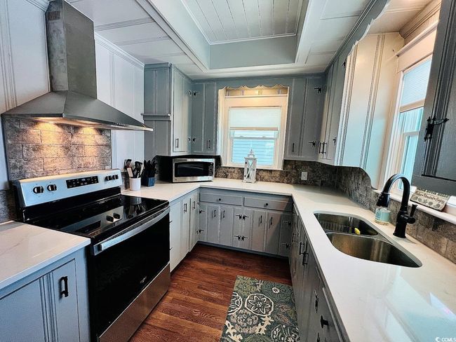 Kitchen featuring dark wood-type flooring, wall chimney exhaust hood, sink, tasteful backsplash, and stainless steel appliances | Image 12