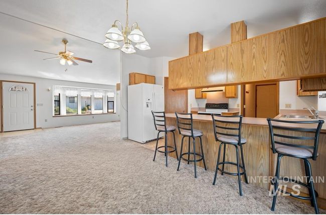 Kitchen with white fridge with ice dispenser, light colored carpet, ceiling fan, a peninsula, and electric range | Image 10