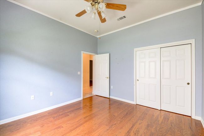 Unfurnished bedroom 2 with ornamental molding, wood finished floors, a closet, ceiling fan, and a high ceiling | Image 21