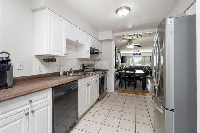 Kitchen featuring backsplash, under cabinet range hood, appliances with stainless steel finishes, light tile patterned flooring, and a sink | Image 14