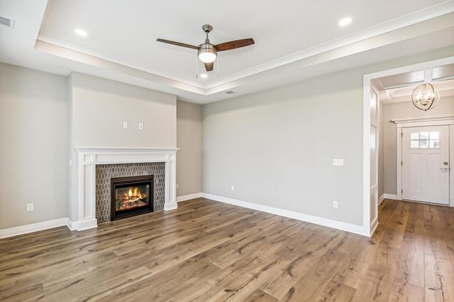 Unfurnished living room with ceiling fan, a raised ceiling, a fireplace, and wood-type flooring | Image 4