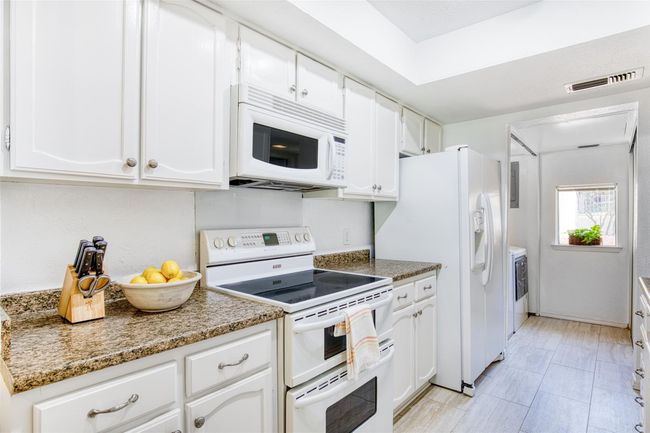 Kitchen featuring white appliances, separate washer and dryer, white cabinetry, and stone counters | Image 14