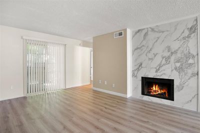 Unfurnished living room featuring a textured ceiling, light hardwood / wood-style floors, and a high end fireplace | Image 1