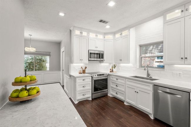 Timeless white kitchen boasts floor-to-ceiling cabinetry, under-cabinet and interior cabinet lighting, a classic subway tile backsplash, and sleek quartz countertops—combining function with elegant design. | Image 7