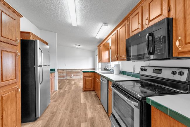Kitchen with stainless steel appliances, a textured ceiling, light wood-type flooring, light countertops, and brown cabinets | Image 16
