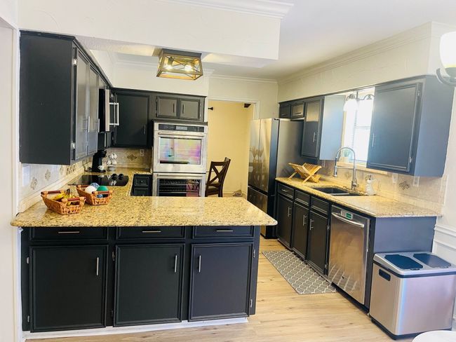 Kitchen with appliances with stainless steel finishes, a sink, dark cabinets, a peninsula, and light wood finished floors | Image 6