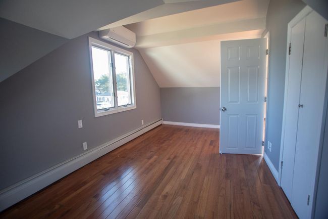 Additional living space with dark hardwood / wood-style floors, lofted ceiling, a wall unit AC, and a baseboard heating unit | Image 21