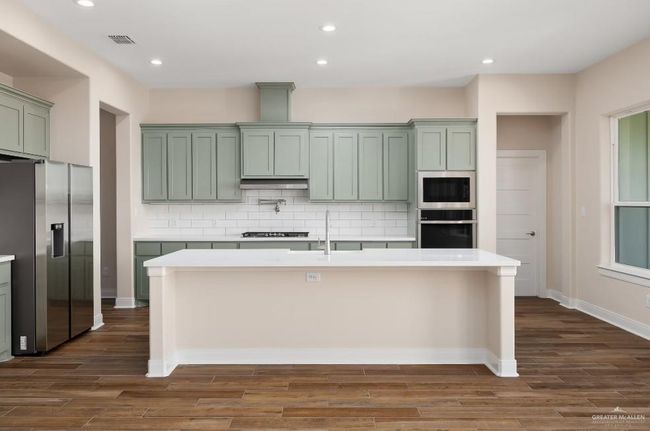 Kitchen featuring green cabinets, built in microwave, black oven, and stainless steel fridge | Image 10