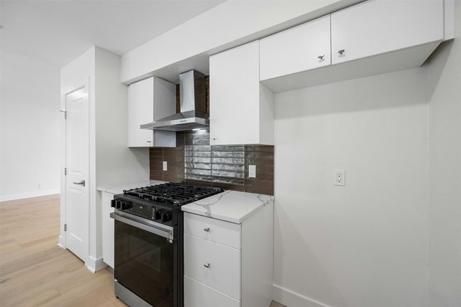 Kitchen with wall chimney range hood, gas range oven, tasteful backsplash, light wood-style floors, and light stone counters | Image 16