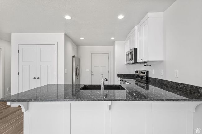 Kitchen with appliances with stainless steel finishes, a sink, a peninsula, dark stone countertops, and white cabinets | Image 12