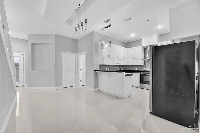 Kitchen featuring stainless steel appliances, light tile patterned floors, white cabinetry, a peninsula, and decorative backsplash | Image 4