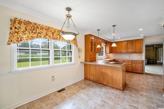 Kitchen with brown cabinets, a sink, a peninsula, decorative backsplash, and baseboards | Image 8