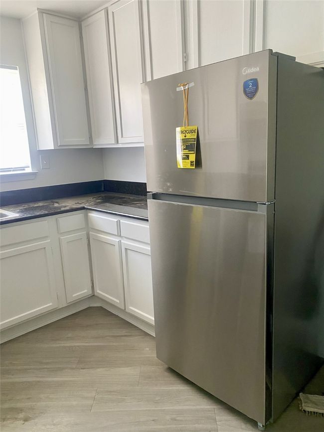 Kitchen featuring freestanding refrigerator, dark countertops, white cabinetry, and light wood-type flooring | Image 7