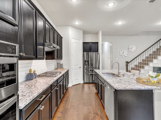 Kitchen featuring appliances with stainless steel finishes, arched walkways, dark wood finished floors, backsplash, and a center island with sink | Image 12