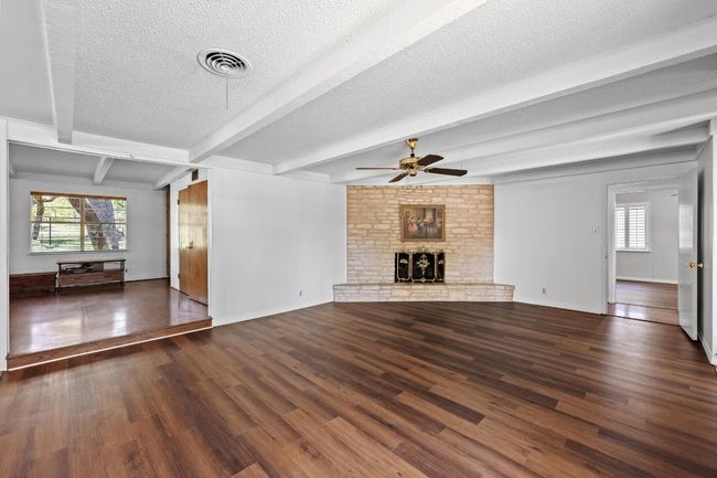 Unfurnished living room featuring ceiling fan, healthy amount of natural light, wood & LVP finished floors, a textured ceiling, and beamed ceiling | Image 6