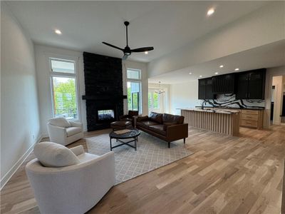 Living room featuring ceiling fan with notable chandelier, a multi sided fireplace, light hardwood / wood-style flooring, and plenty of natural light | Image 3