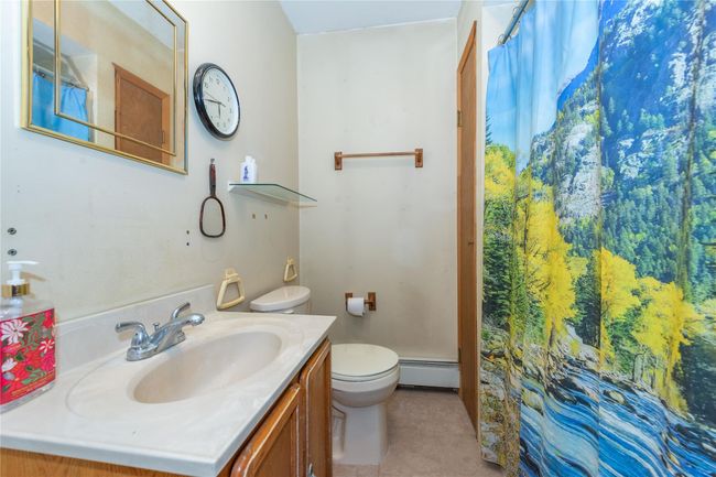 Bathroom featuring curtained shower, toilet, a baseboard heating unit, vanity, and tile patterned flooring | Image 36