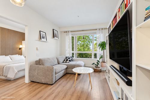 Open-concept living area featuring wood-finish flooring, a large window, and built-in shelving with integrated media storage | Card Image