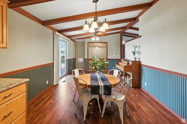 Dining space with a wainscoted wall, a chandelier, dark wood-style flooring, and beam ceiling | Image 11