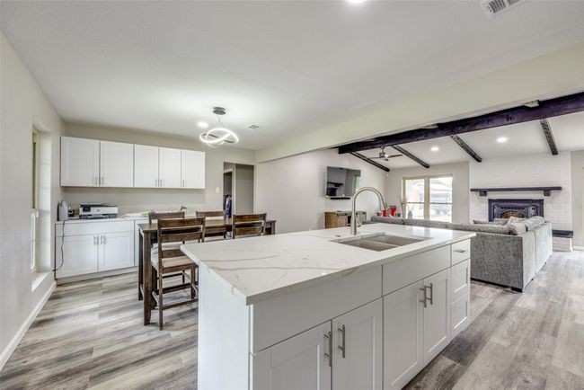 Kitchen featuring light wood finished floors, white cabinetry, open floor plan, light stone counters, and beam ceiling | Image 15