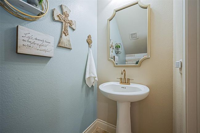 This elegant powder room showcases a pedestal sink accented by modern gold hardware, complemented by a framed mirror and a decorative accent wall. | Image 28