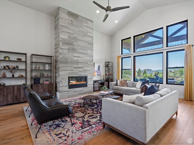 Living area with high vaulted ceiling, a tile fireplace, ceiling fan, wood finished floors, and recessed lighting | Image 8