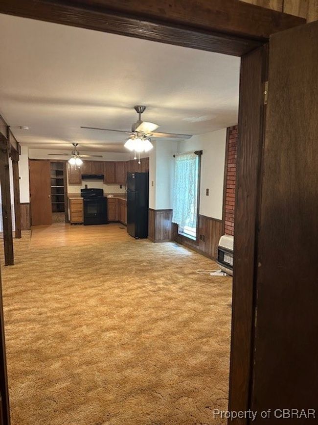 Unfurnished living room featuring light colored carpet, wainscoting, ceiling fan, heating unit, and wooden walls | Image 10