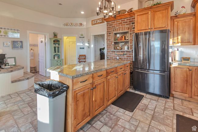 Kitchen featuring pendant lighting, backsplash, a chandelier, stainless steel refrigerator, and light stone counters | Image 34