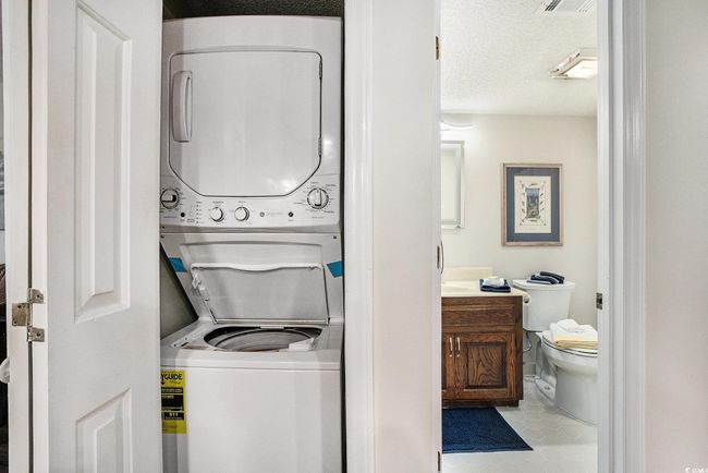 Laundry area with a textured ceiling, stacked washer / dryer, and light tile patterned floors | Image 12