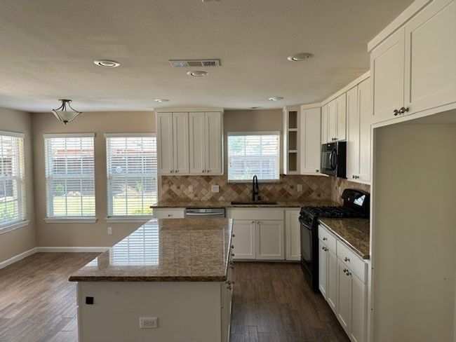 Kitchen featuring black appliances, dark stone countertops, backsplash, white cabinetry, and a center island | Image 4